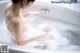 A woman in a white bra sitting in a bathtub.