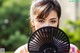 A woman holding a black fan in front of her face.