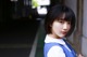 A young woman in a school uniform leaning against a wall.