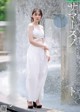 A woman in a white dress standing in front of a fountain.